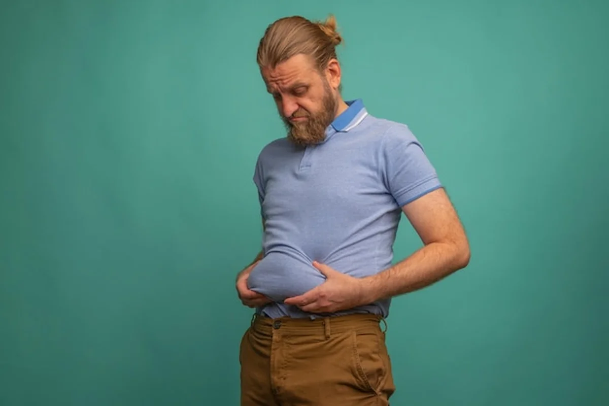 Mężczyzna z smutną twarzą trzyma gruby brzuch