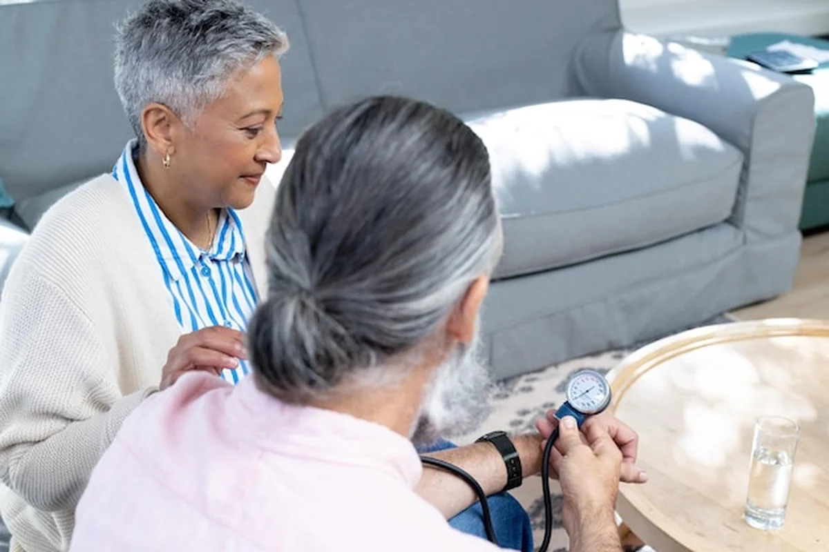 Starsza para mierzy ciśnienie na kanapie w salonie