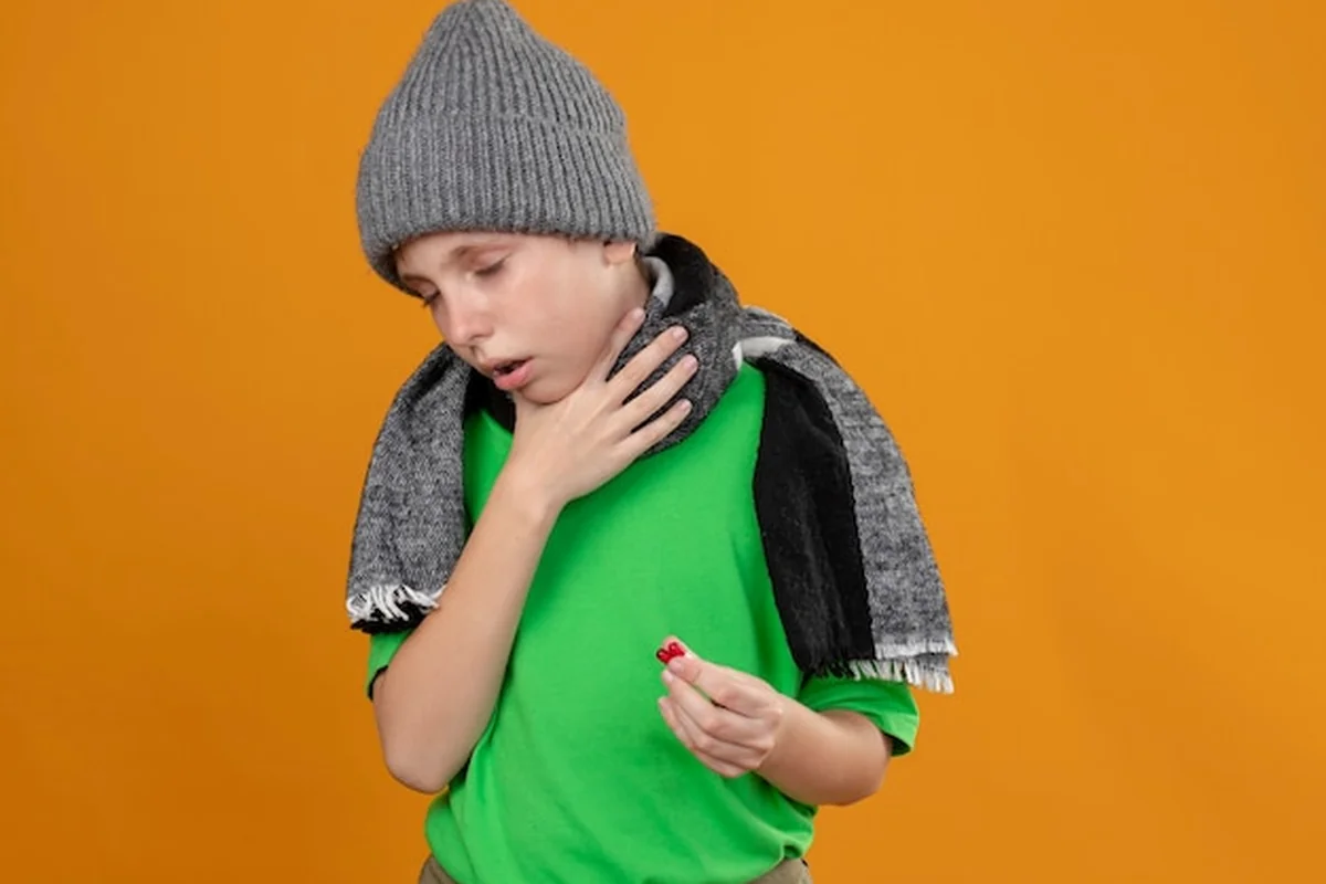 Chory chłopiec w zielonej koszulce trzymający pigułki przed pomarańczową ścianą