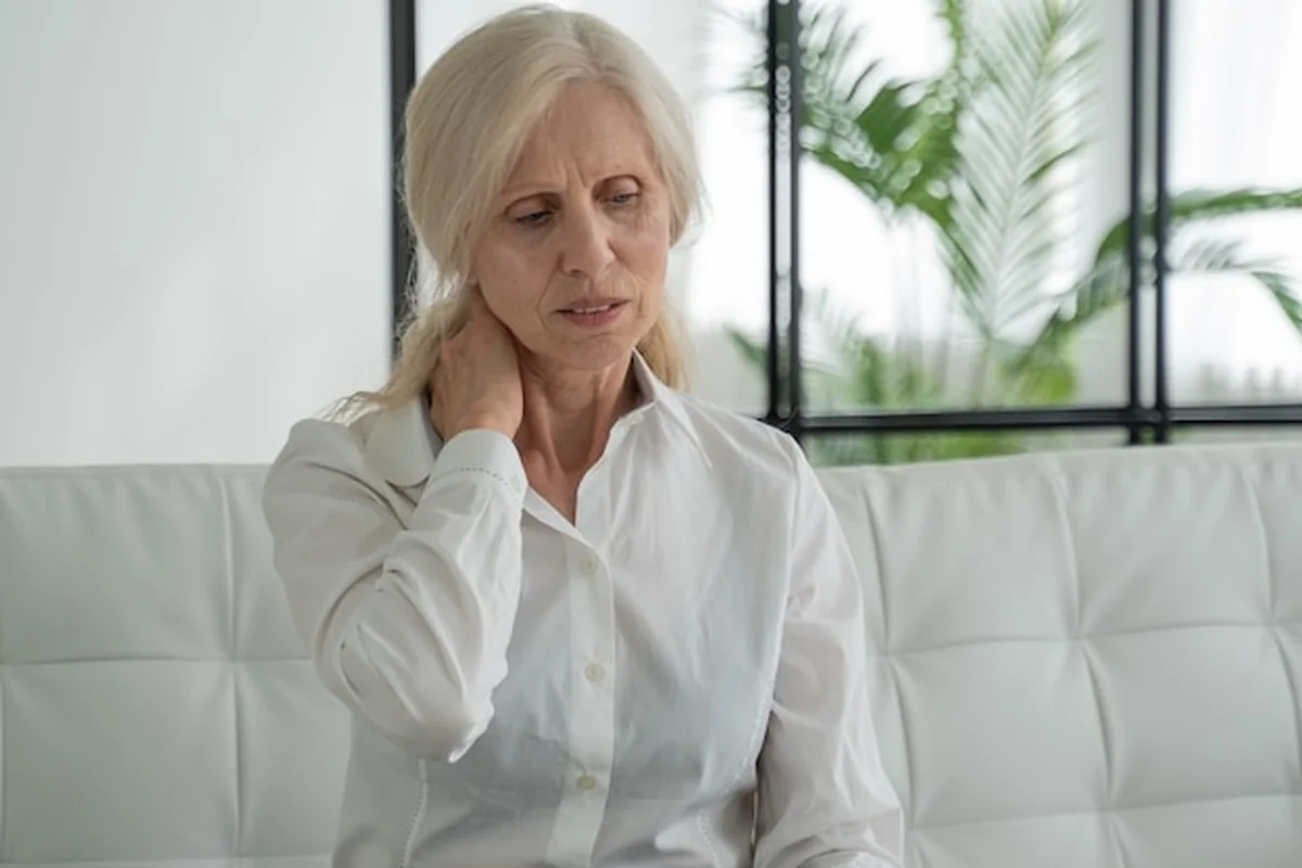 Starsza kobieta cierpiąca na ból szyi siedząca na kanapie w domu