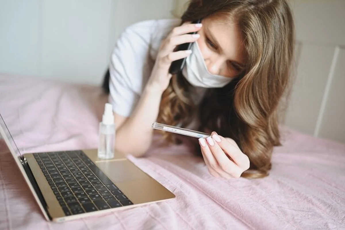 Chora kobieta w masce leży w łóżku z laptopem i termometrem