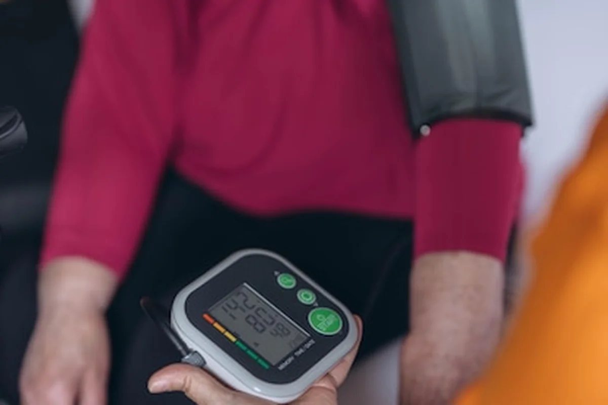 Starsza kobieta siedzi na łóżku podczas pomiaru ciśnienia krwi